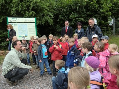 Bild: Revierleiter Spindler (links) erklärt den Kindergartenkindern die Arbeit eines Försters und Waldarbeiters